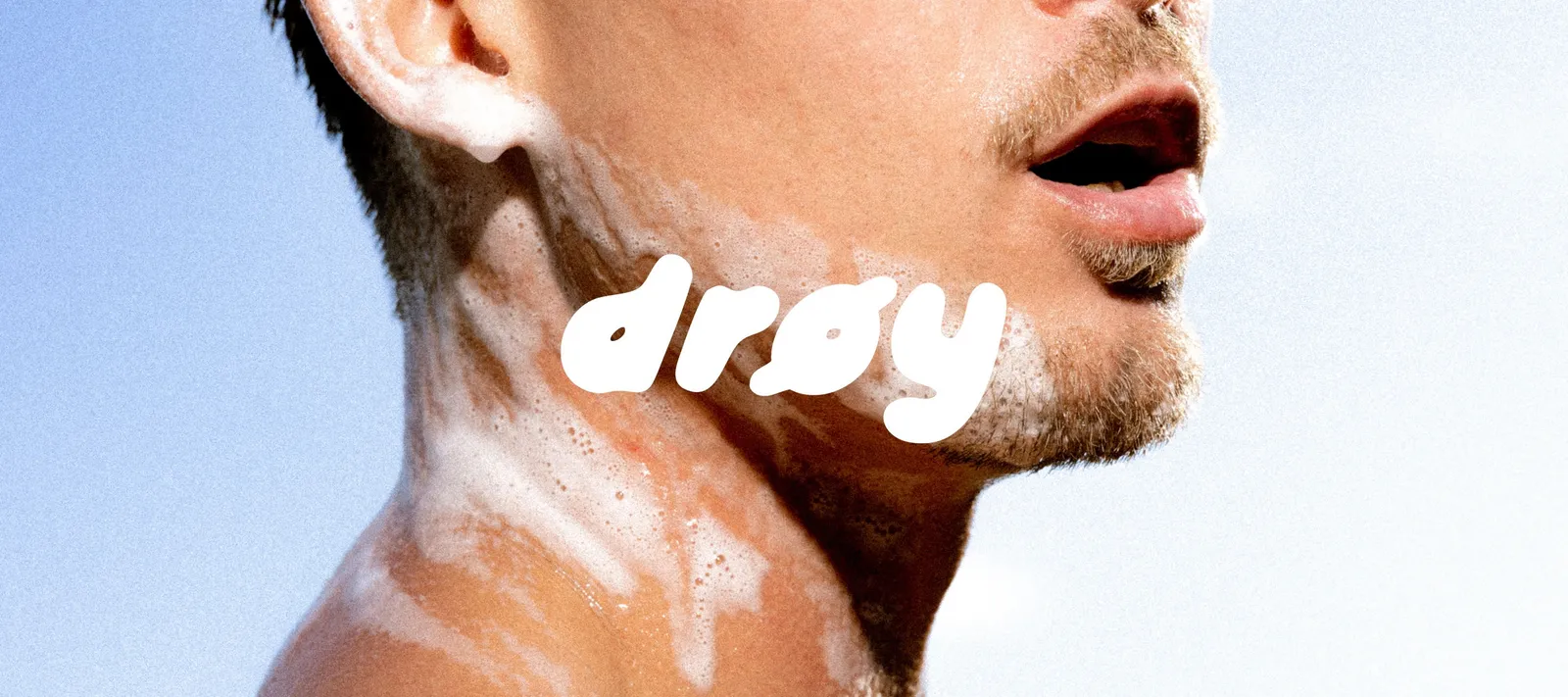 DRØY-logoen i hvitt over en hals med skum, mot blå himmel
